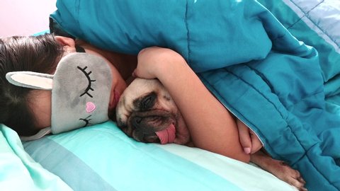 Young woman wear eyes mask is lying down and sleeping rest with pug dog puppy in bed. Nap with hugging dog