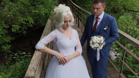 Beautiful bride and groom on an old iron bridge in the forest. Groom caresses his beloved.