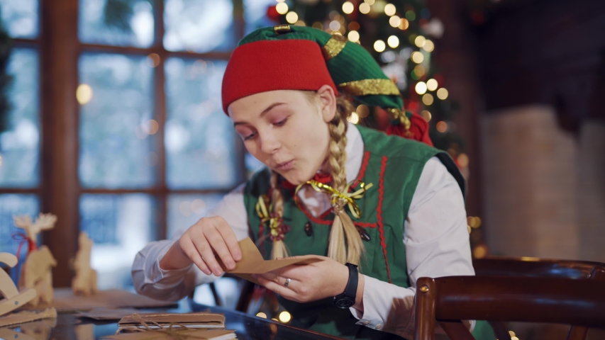 Curious elf looking inside the envelope for Santa. Christmas interior cute female elf sits at the table with envelope.