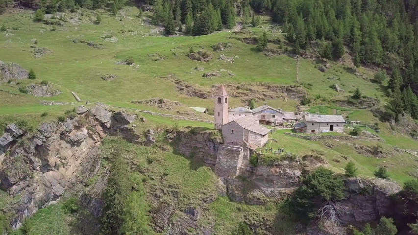 4k aerial view circling around Christian church or chapel close to cliff drop-off above mountain valley in Val Poschiavo Switzerland. Medium wide circling cinematic epic 