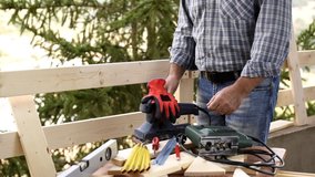 Adult carpenter craftsman with electric sander smoothes the boards of a wooden fence. Housework do it yourself. Footage.