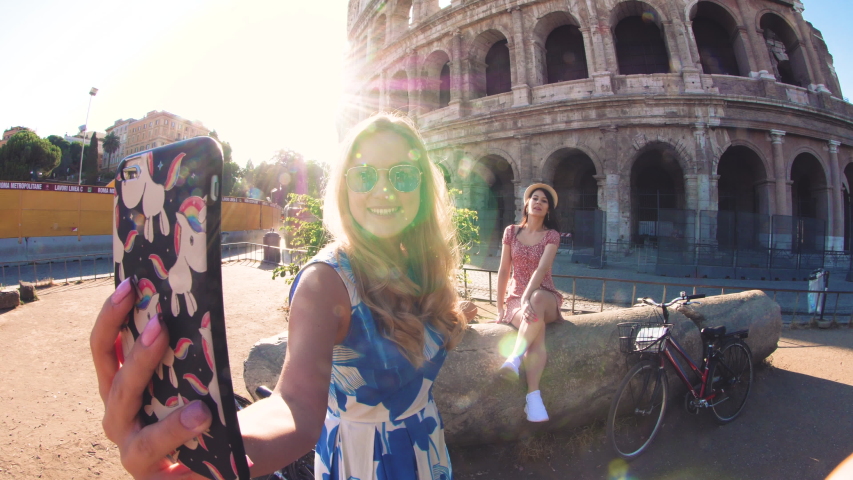 Three happy young women friends tourists with bikes taking videos with smarphone at Colosseum in Rome, Italy at sunrise. Royalty-Free Stock Footage #1037615696