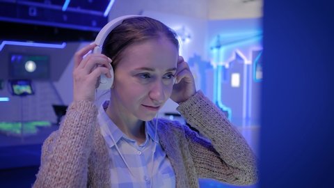Woman looking at exposition, using white headphones and listening audio guide at modern futuristic exhibition or museum. Education, sci-fi, interactive, technology, future and entertainment concept