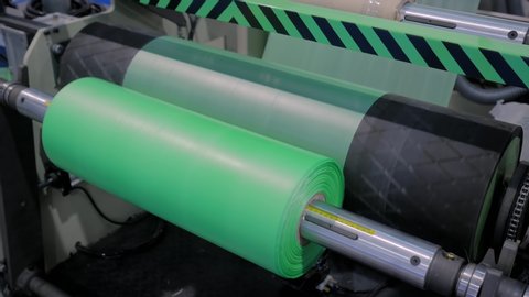 Manufacturing, recycling, industry and automated technology equipment concept. Part of automatic plastic bag making machine - moving roller with flat polyethylene green film at exhibition, trade show