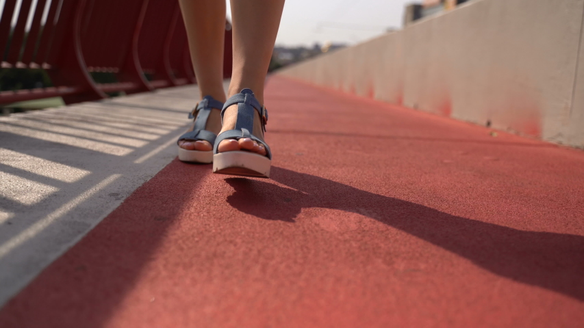 Female legs walk on a footpath on a bridge