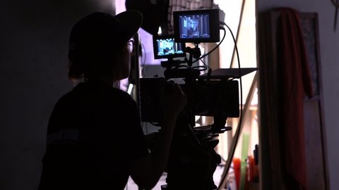 Movie Making Back View of Cameraman Shooting Film. Professional Filmmaker Woman Working with Camera at Dark Studio. Television Scene Production. Female Operator. Footage Shot Full HD 1080p