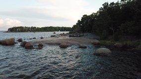 4K summer morning aerial video of northern cold sea wild lagoon in northern hemisphere in Scandinavia, pine tree forest beach, red granite boulders and lone island with small boats, northern Europe