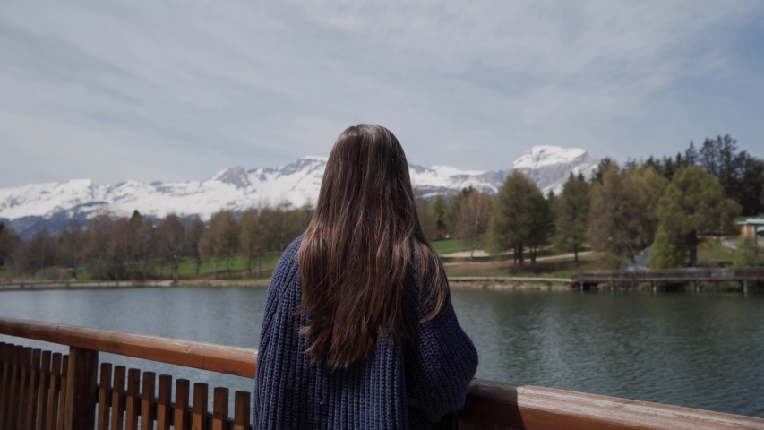 Long-hair brunette woman standing and looking scenic view of mountain lake in Switzerland. Rear view. Focus on female hair