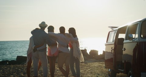 Slow motion of group of young multi-ethnic friends just arrived with a minivan are having fun to start a vacation a beach with a sea on a sunset.