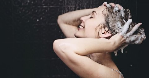 Woman taking shower in slow motion. Filmed in 4K DCi resolution. Young beautiful woman taking a shower and washing her hair with a shampoo, smiling. Beauty and wellbeing concept.