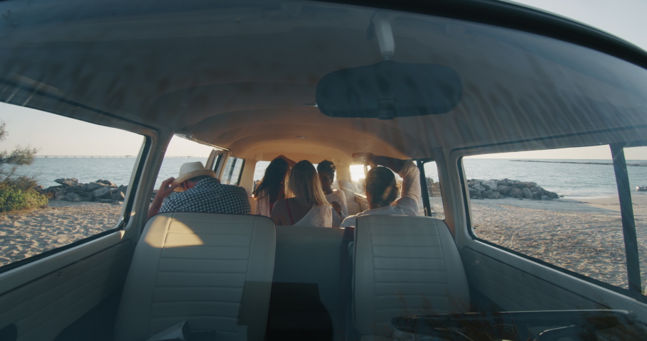 Slow motion of group of young multi-ethnic friends just arrived with a minivan are happy to start their vacation  and having fun on a beach with a sea on a sunset. Royalty-Free Stock Footage #1037631422