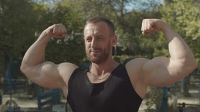 Handsome brutal muscular bodybuilder with perfect abs, shoulders, triceps and chest showing well trained body while standing in double biceps pose on outdoor sport facilities, expressing confidence. - Powered by Shutterstock - Get 15% off with code: PIKWIZARD15