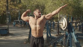 Handsome shirtless motivated muscular bodybuilder with perfect trained body showing classic front double biceps pose in outdoor gym, outstretched his arm and looking away while posing outdoors. - Powered by Shutterstock - Get 15% off with code: PIKWIZARD15