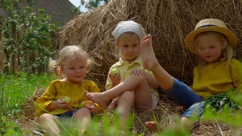 Three little girls having fun, laughing and playing feet on a haystack