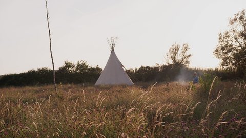 Evening Shot Of Mature Friends Sitting Outside Teepee As They Camp In Countryside Field