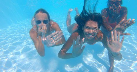Underwater shot of young multi-ethnic girlfriends in bikinis are having fun to enjoy their summer in swimming pool and smiling in camera.