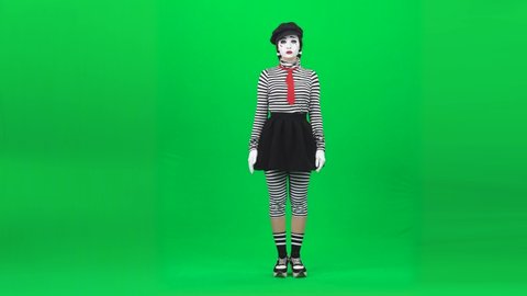 Mime girl with professional make-up, dressed in striped turtleneck and leggings, black skirt and hat, is putting her hands on an invisible glass, dancing and playing piano. Chroma key. Full length.