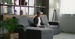 Young woman enjoys 360 video in virtual reality headsets, using gestures to control images, sitting on a sofa in living room. Slow motion, General plan, 4K, shot on RED camera.