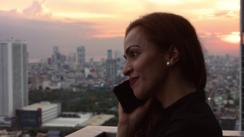 young red-haired woman on the phone with in the background a sunset over the city and the building, Manila Philippines