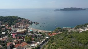 Low flying aerial drone footage of vacationing tourists, waves and sunshine on the beautiful shores and sandy beach of landmark Budva. Sea waves roll in the seashore