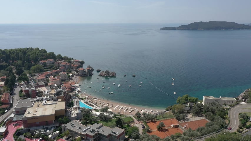 Low flying aerial drone footage of vacationing tourists, waves and sunshine on the beautiful shores and sandy beach of landmark Budva. Sea waves roll in the seashore