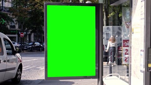 Green screen bus stop advertising, billboard ad next to a tree in a busy city center street of Paris during a sunny afternoon