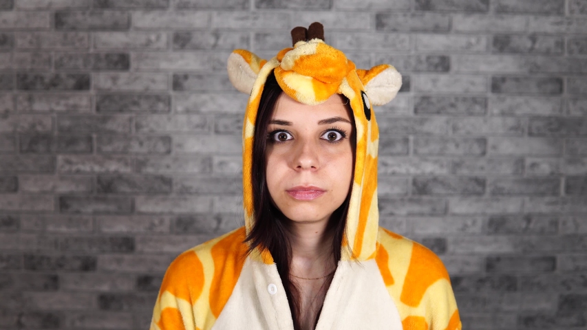 A funny woman in a big kigurumi of giraffe shows a stop sign which expressing protest on a gray brick background in the studio.