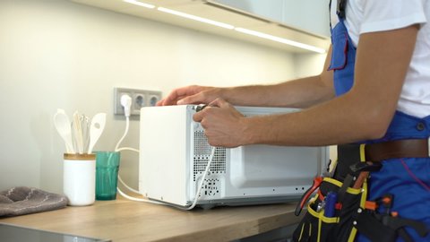 Man in uniform repairing microwave using screwdriver, maintenance guarantee