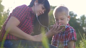 happy family funny video play music slow motion teamwork outdoors. Mom and son listen to music on smartphone in the same headphones for two. happy family mother woman and lifestyle son little boy
