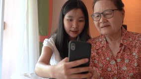 Asian pretty niece teaching her grandmother to using smartphone and new technology feeling happy and smiling, family concept    