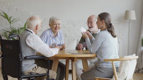 Group of four retired senior people, two men and two women, having fun sitting at table and playing cards together in common room of nursing home, tracking shot - Powered by Shutterstock - Get 15% off with code: PIKWIZARD15