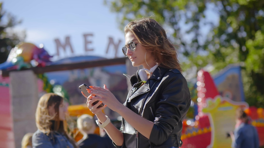 Side view of young caucasian woman that buys electronic tickets for attractions with a help of smartphone in park. Digital purchase concept