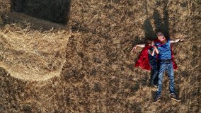 Straight down view of imaginary superheroes talking while lying in the middle of mowed wheat field. Aerial shot of playful dad and son in superhero costumes relaxing in nature during summer vacation - Powered by Shutterstock - Get 15% off with code: PIKWIZARD15