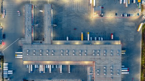 Aerial top view of the large logistics park with warehouse, loading hub with many semi-trailers trucks standing at the ramps for load/unload goods at night. Hyper lapse (time lapse)