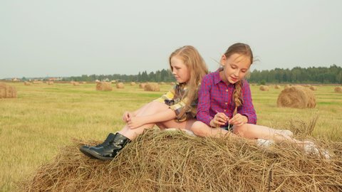 Teenager girl sitting on peak hay stack. Serious girl teenager thinking on hay stack at harvesting field. Girl friends relaxing on farmland field