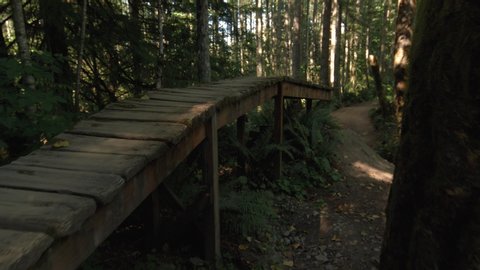 Camera Follows Mountain Bike Tires Riding Wood Obstacle to Drop on Forest Trail