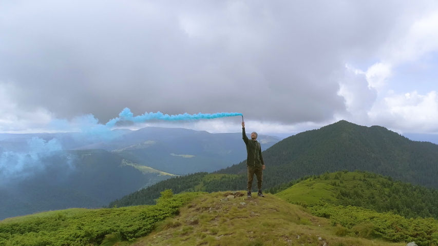 The male with a smoke bomb standing on the picturesque mountain