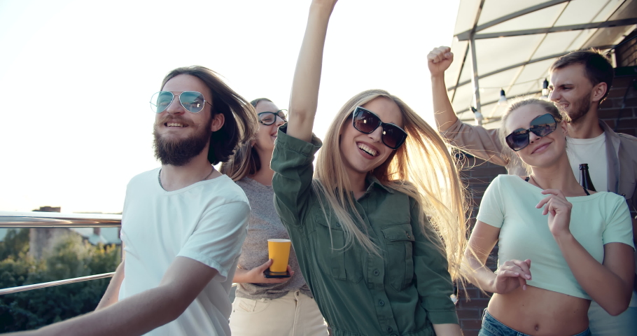 Group of happy stylish youth dancing on rooftop party and smiling to camera, enjoying good time