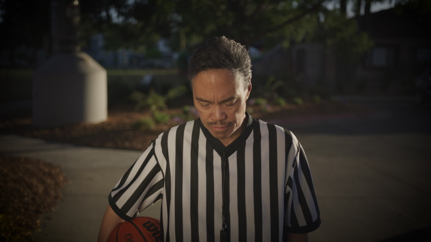 Asian Referee with basketball standing looking into camera slow motion
