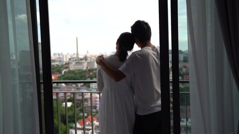 Beautiful young Asian couple spending time together on balcony with city views, Urban condominium. 