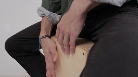 Detail shot of a young gypsy styled man hands playing cajon flamenco drumbox having fun rehearsing and creating percussion sounds on a home studio background.