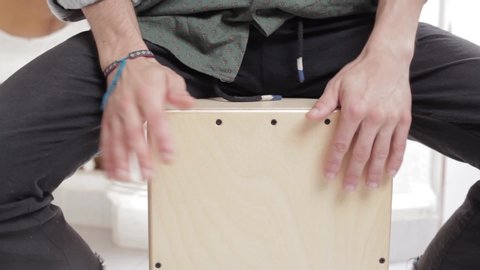 Detail shot of a young gypsy styled man hands playing cajon flamenco drumbox having fun rehearsing and creating percussion sounds on a home studio background.