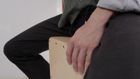 Detail shot of the hands of a young gypsy styled man hands playing cajon flamenco drumbox having fun rehearsing and creating percussion sounds on a home studio background. 