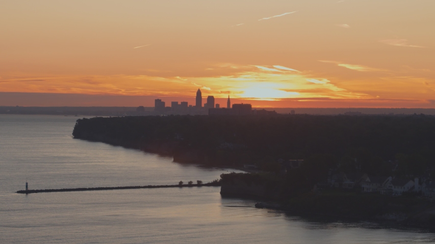Aerial dolly shot of a silhouetted downtown Cleveland Ohio at sunrise from above Lake Erie with pier in foreground