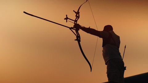 Man shoots a bow. Archery silhouette, sun sets behind the archer