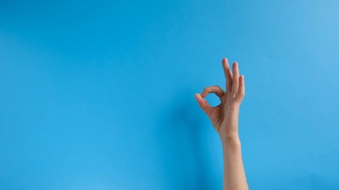 Unrecognizable female shows an ok sign on wall blue background.  Hand sign. Body language and meditation concept. With place for text or image, promotional content.