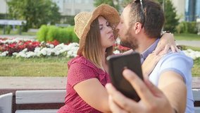 Young couple taking a selfie portrait while relaxing in a city park. Happy lovers want to capture a pleasant moment. Slow motion