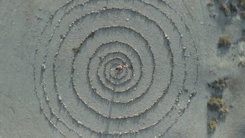 aerial top view of young woman in the center of a spiral stone path labyrinth, argentiera sardinia