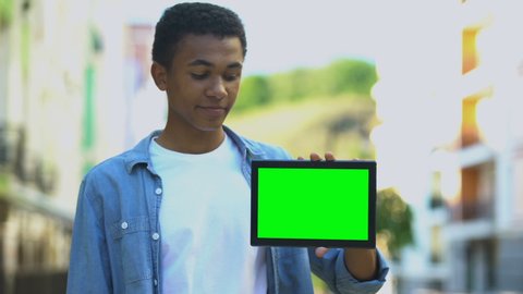 Excited black boy pointing finger at green screen tablet in hand, advertising