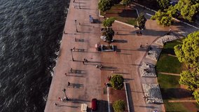 beautiful aerial drone video of thessaloniki's sealine with people walking and waves hitting the stones